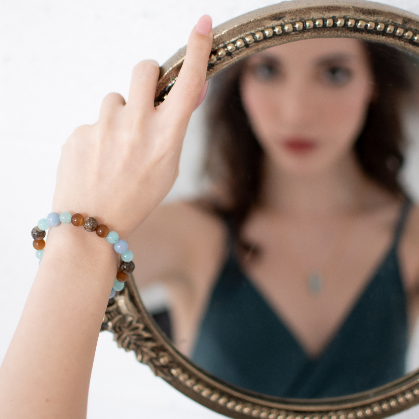 Woman holding a round mirror with a beaded bracelet on her wrist