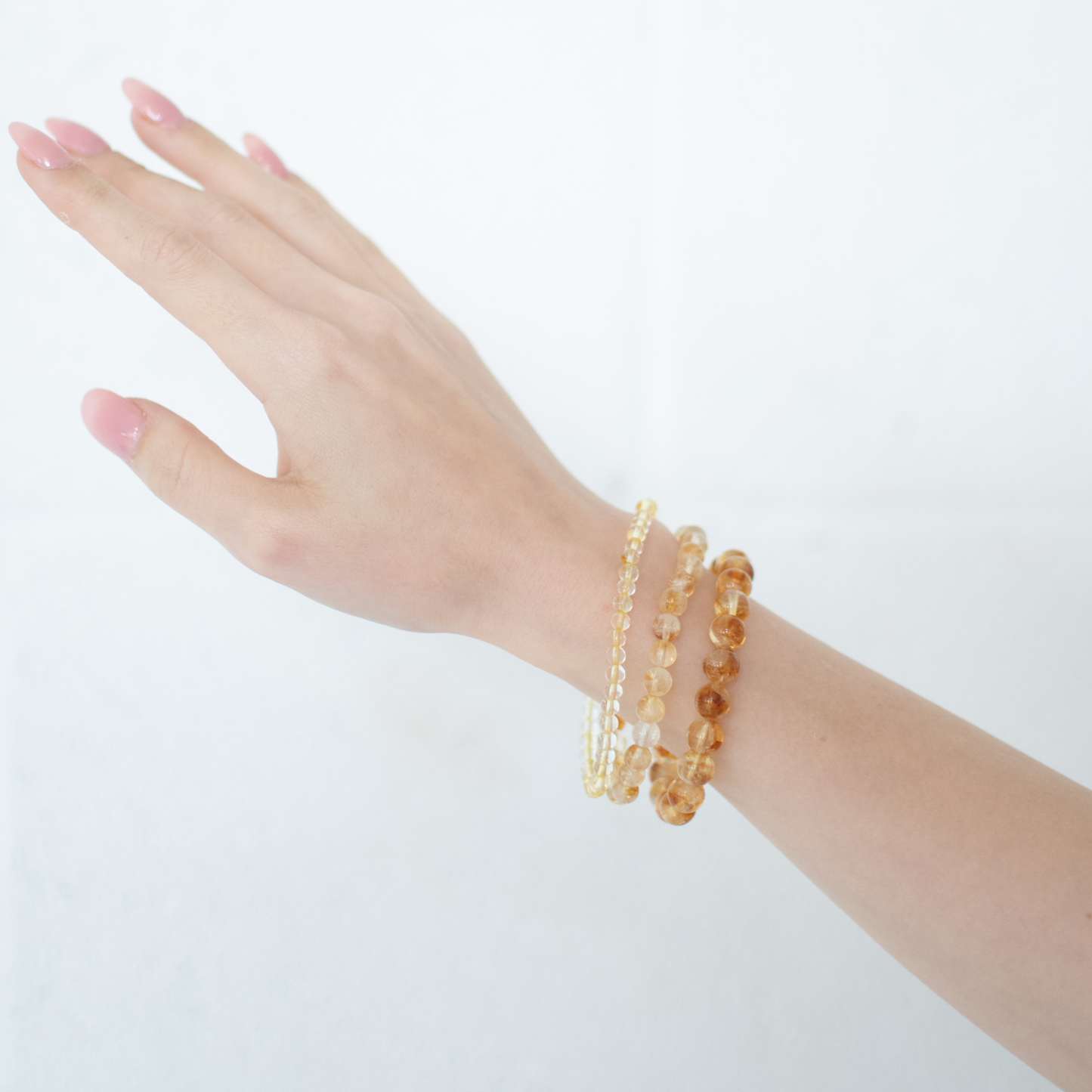 Hand wearing multiple beaded bracelets on a plain background