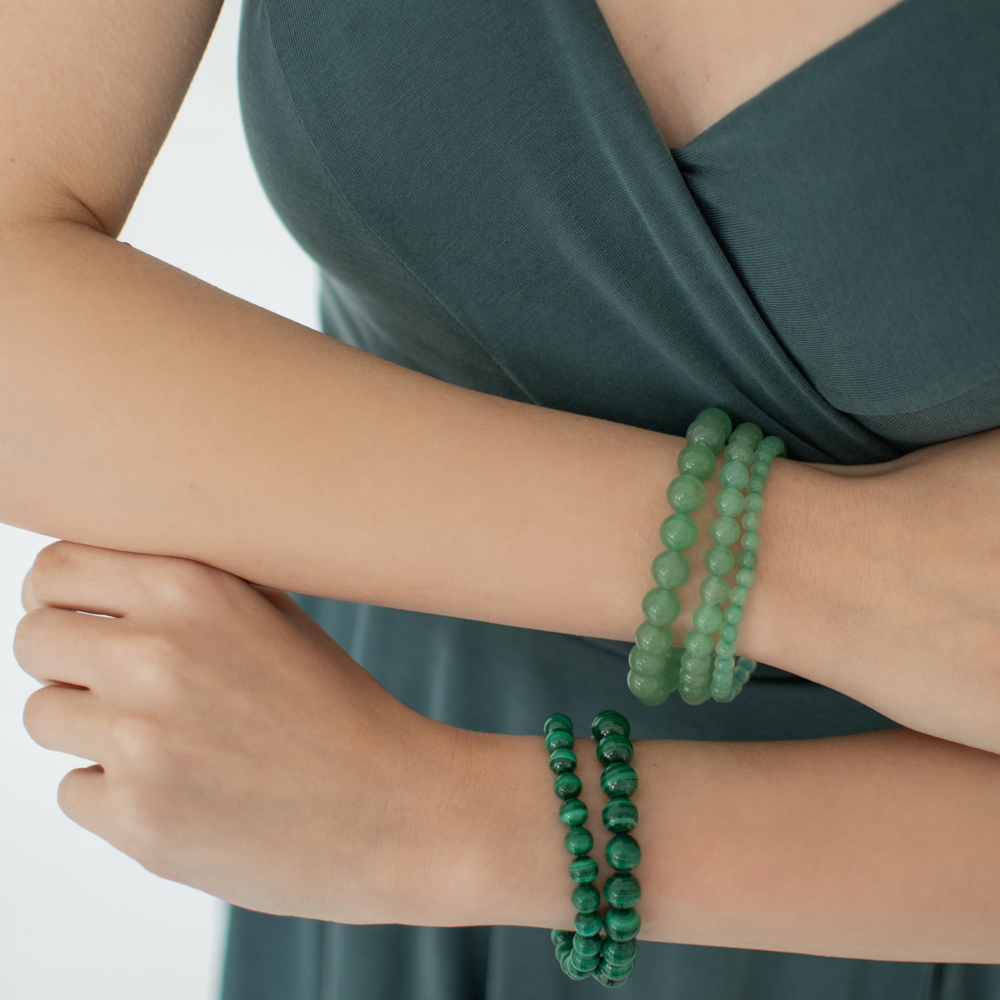 Person wearing green beaded bracelets on a plain background