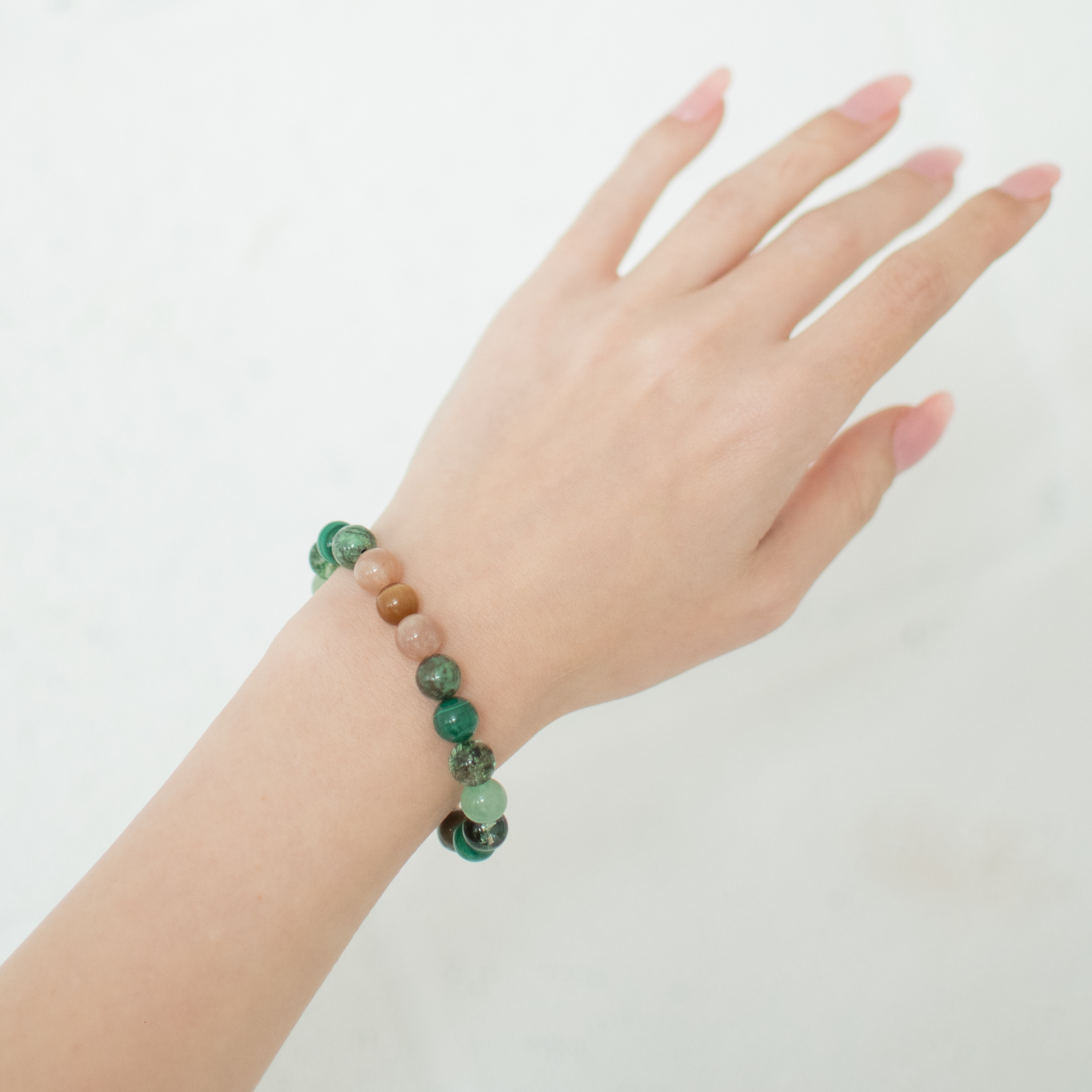 Hand wearing a bracelet with green beads on a plain background
