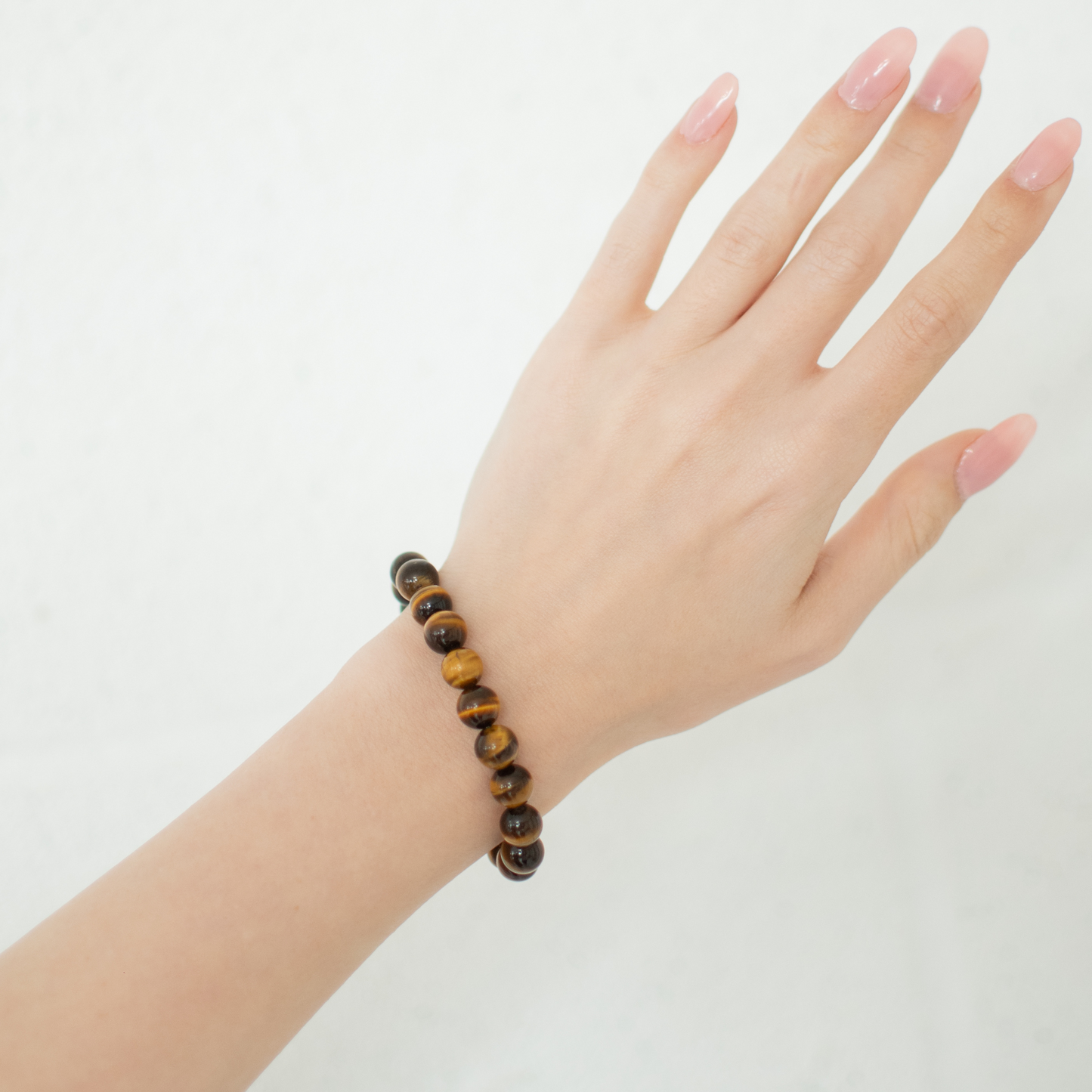 Hand wearing a tiger eye bracelet on a plain background