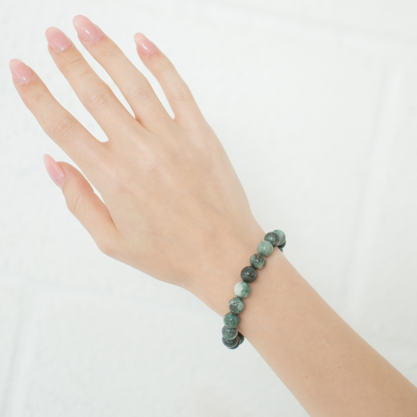 Hand wearing a green beaded bracelet on a white background