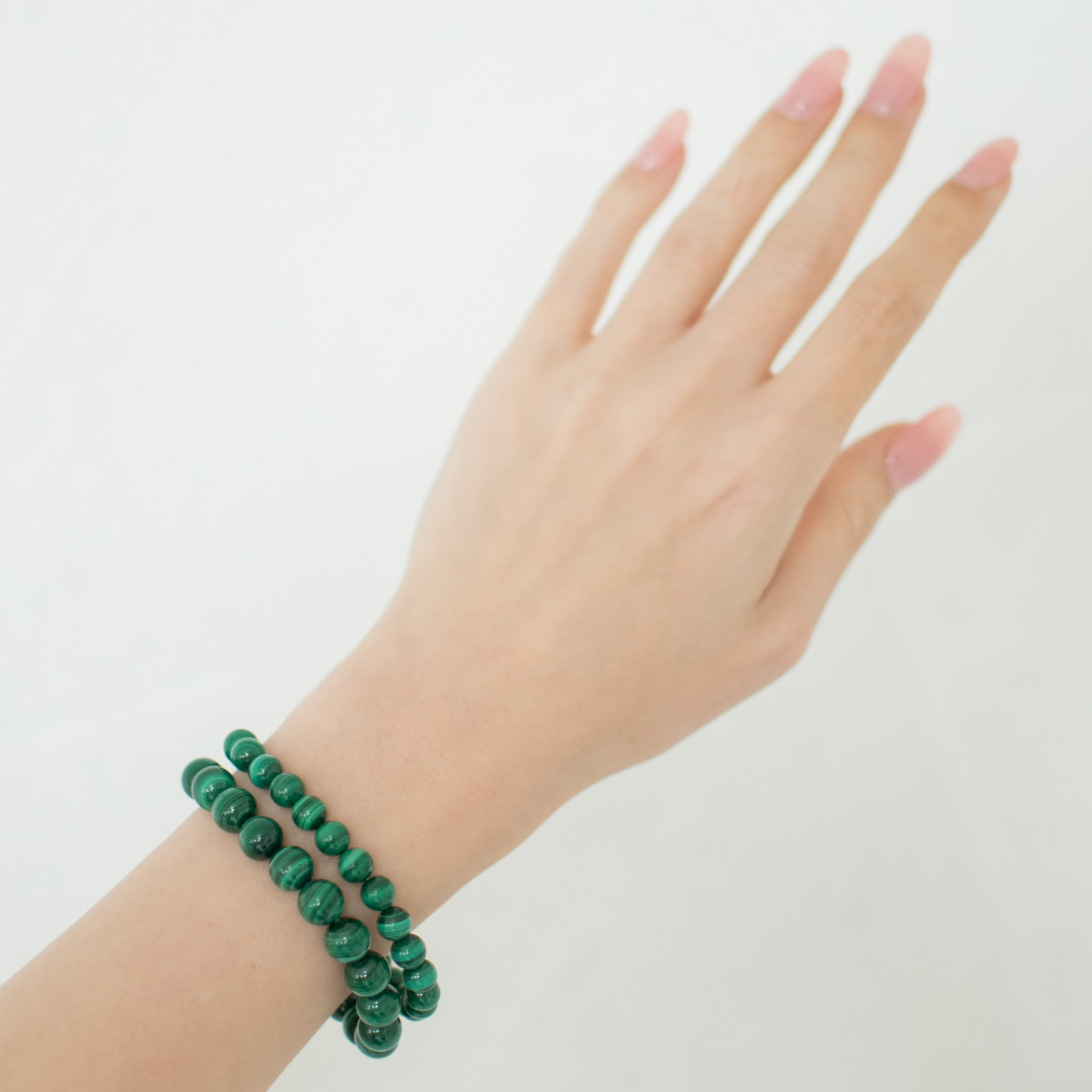 Hand wearing two green beaded bracelets on a white background