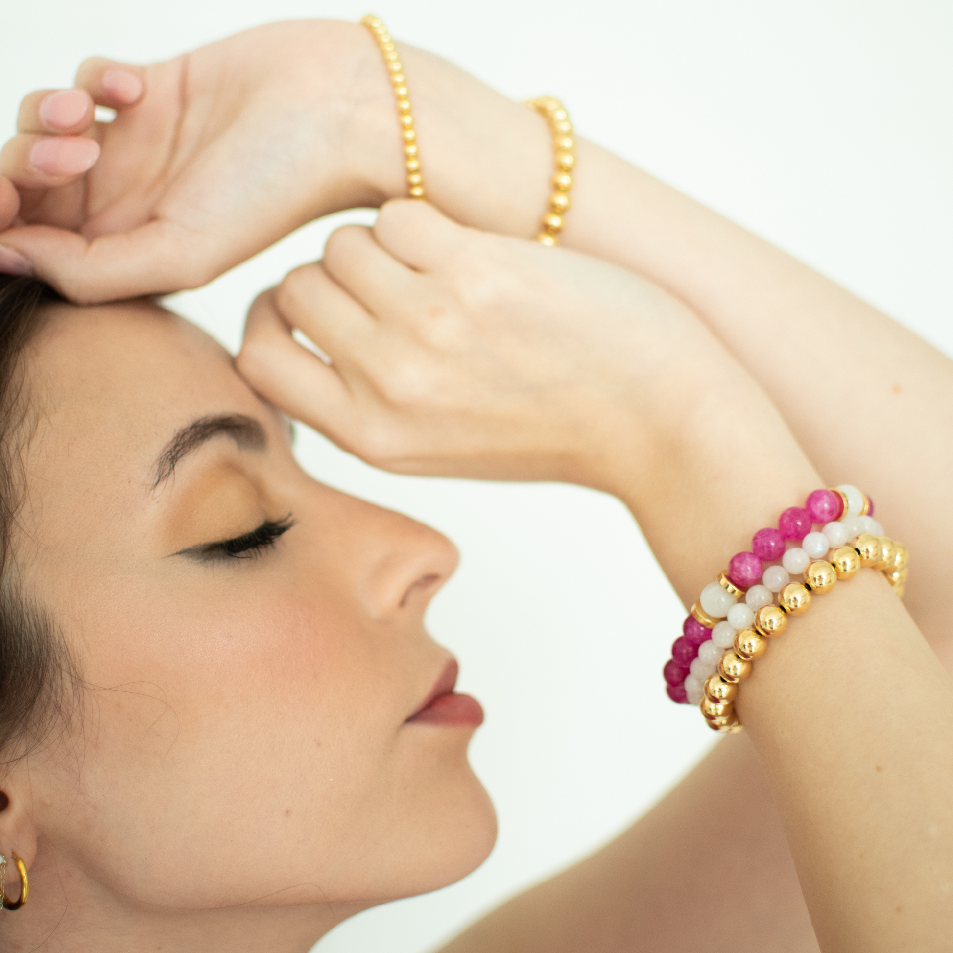 Woman wearing gold and beaded bracelets on a white background